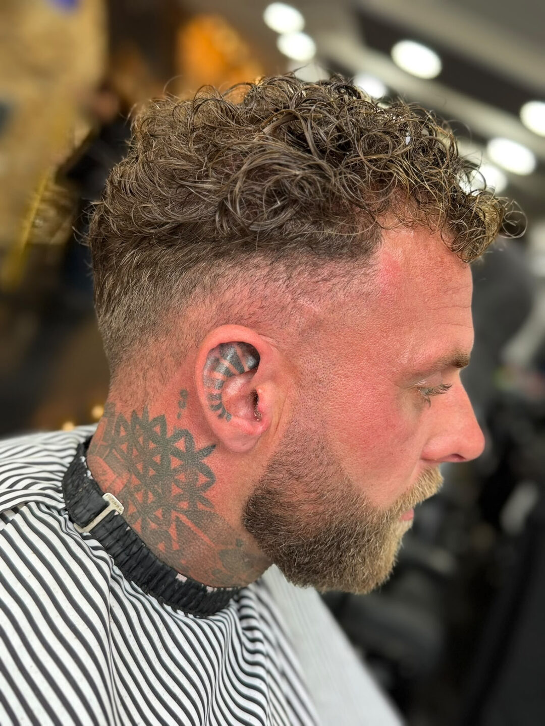 Herenknipbeurt in profiel: krullend haar bovenop met strakke overgang en gekleurde baard